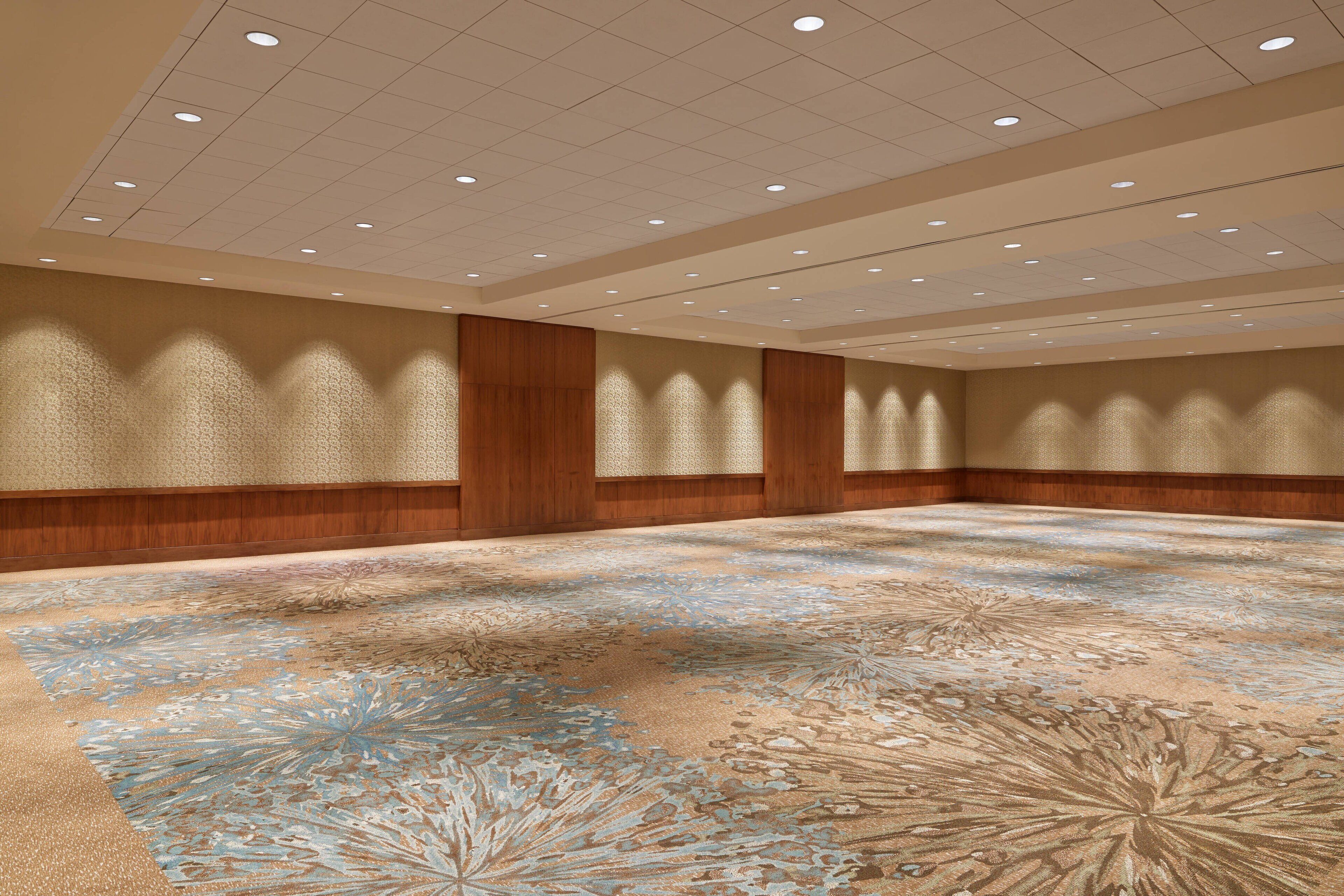 A large, empty conference room with a patterned carpet, wooden paneling, and recessed lighting.