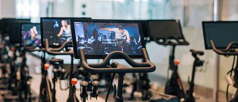 A row of stationary bikes with screens displaying a person performing.