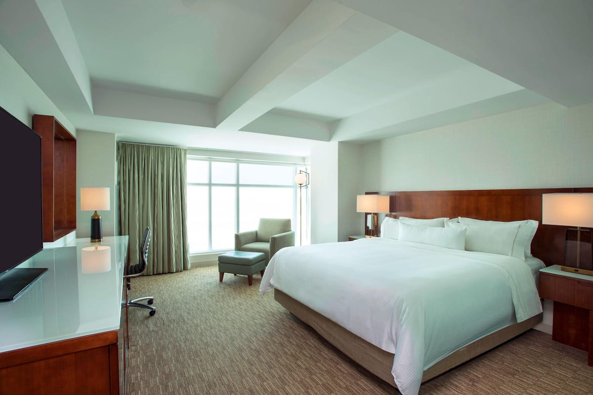A hotel room with a large bed, a desk with a computer, a chair, and a window with curtains.