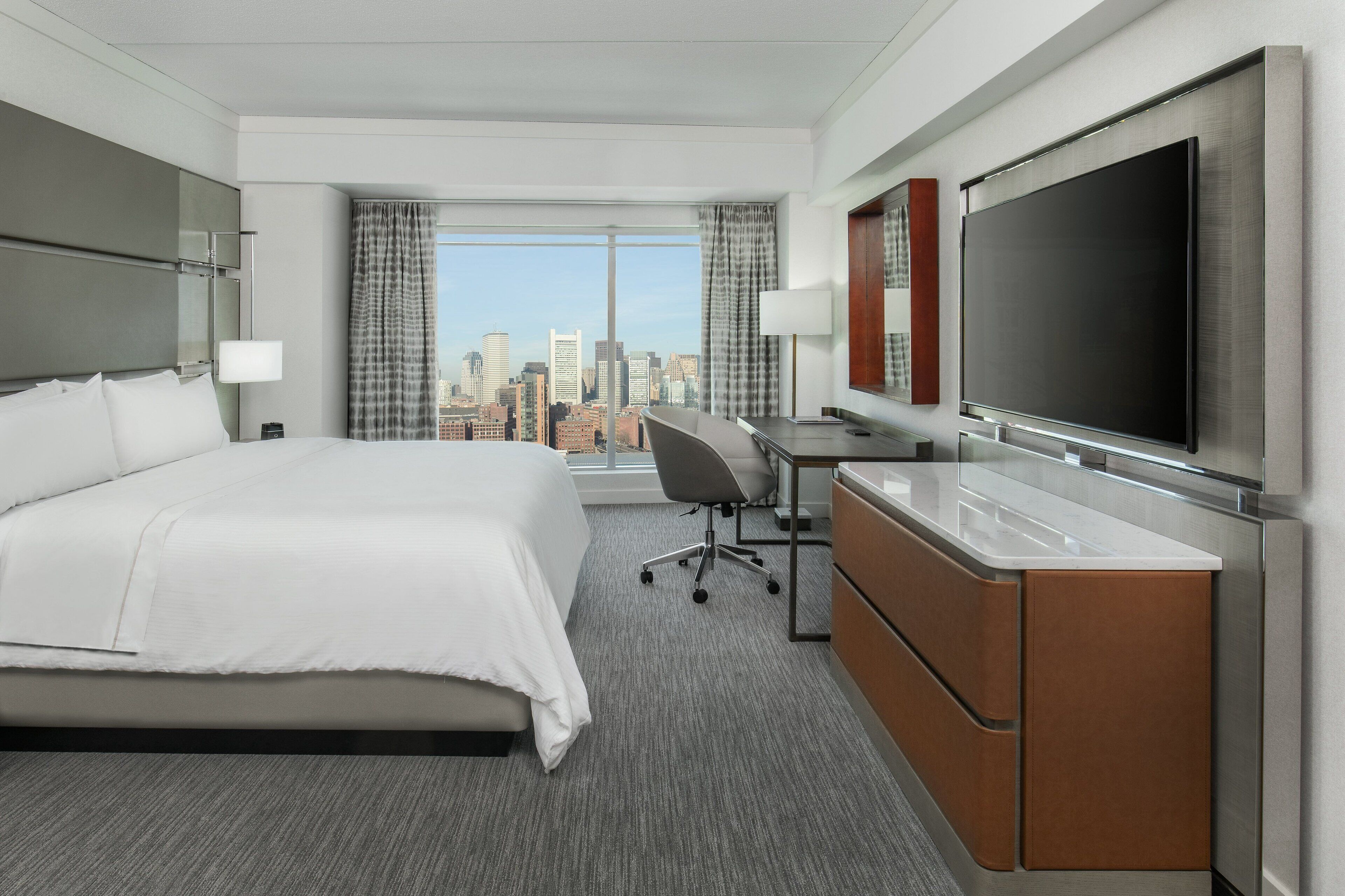 Habitación de hotel con una cama grande, un escritorio, un televisor de pantalla plana y vistas a la ciudad.