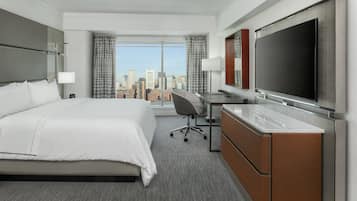Habitación de hotel con una cama grande, un escritorio, un televisor de pantalla plana y vistas a la ciudad.