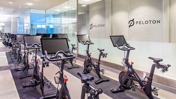 Varias bicicletas estáticas Peloton en un gimnasio moderno con paredes de vidrio y un diseño limpio y minimalista.