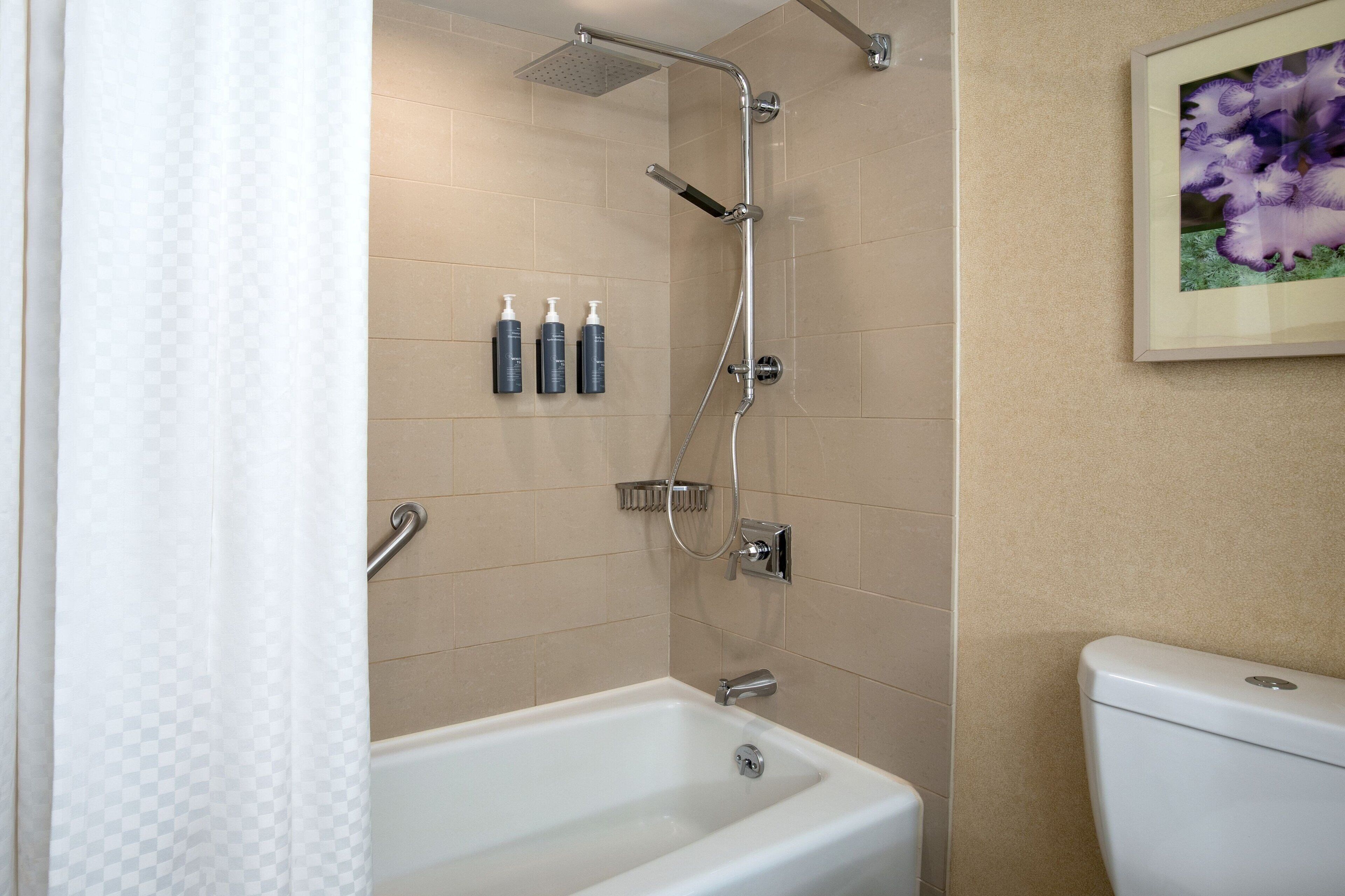 A bathroom with a bathtub, shower, and toilet. There are three bottles of toiletries on the wall.