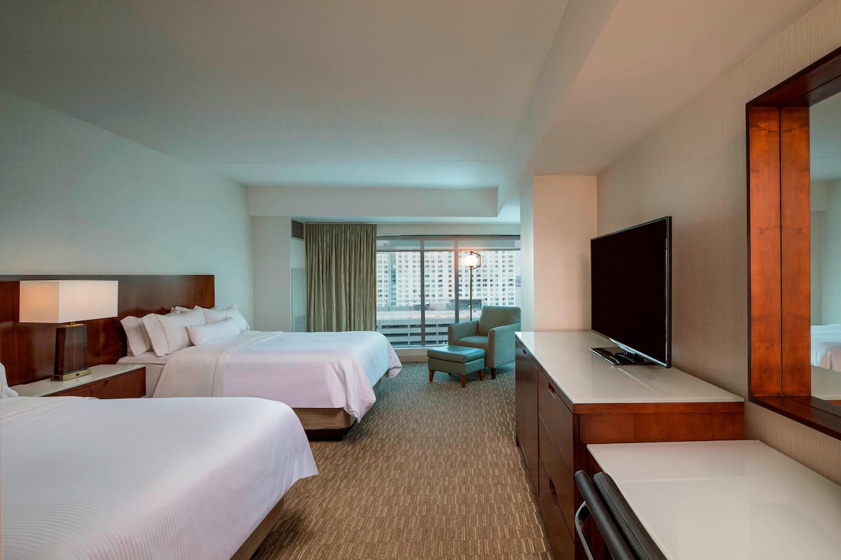 A hotel room with two beds, a desk with a flat-screen TV, a chair, and a large mirror.