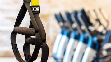 A TRX suspension trainer with a yellow handle, surrounded by other fitness equipment.