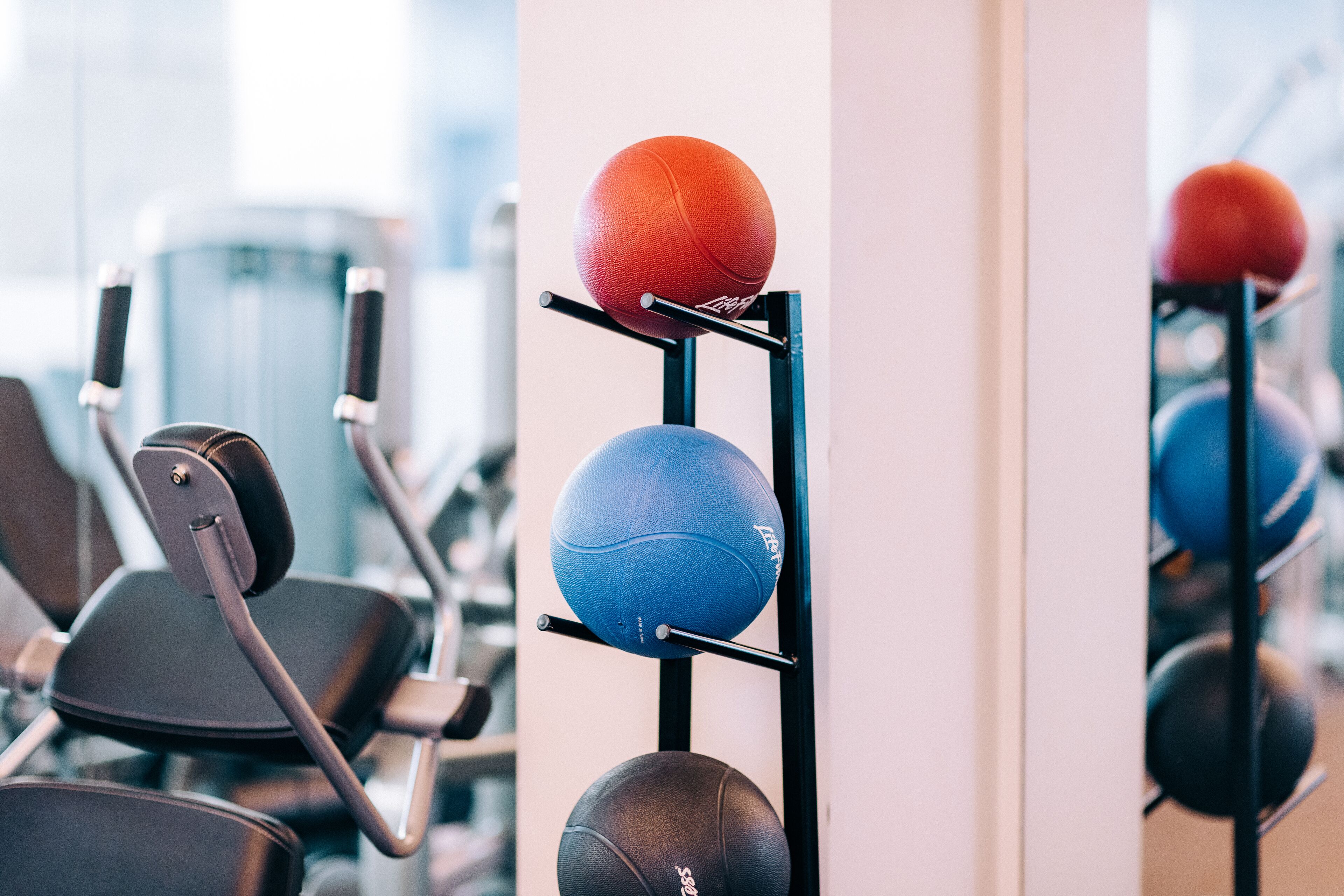 Un gimnasio con equipamiento de ejercicio y un estante de balones deportivos.