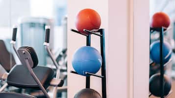 Un gimnasio con equipamiento de ejercicio y un estante de balones deportivos.