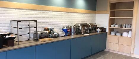 A buffet setup with a self-service station, a coffee machine, and a variety of food containers.
