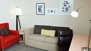 Een hotelkamer met een rode fauteuil, een beige bank, een kleine tafel, een lamp en kunstwerken in lijsten aan de muur.