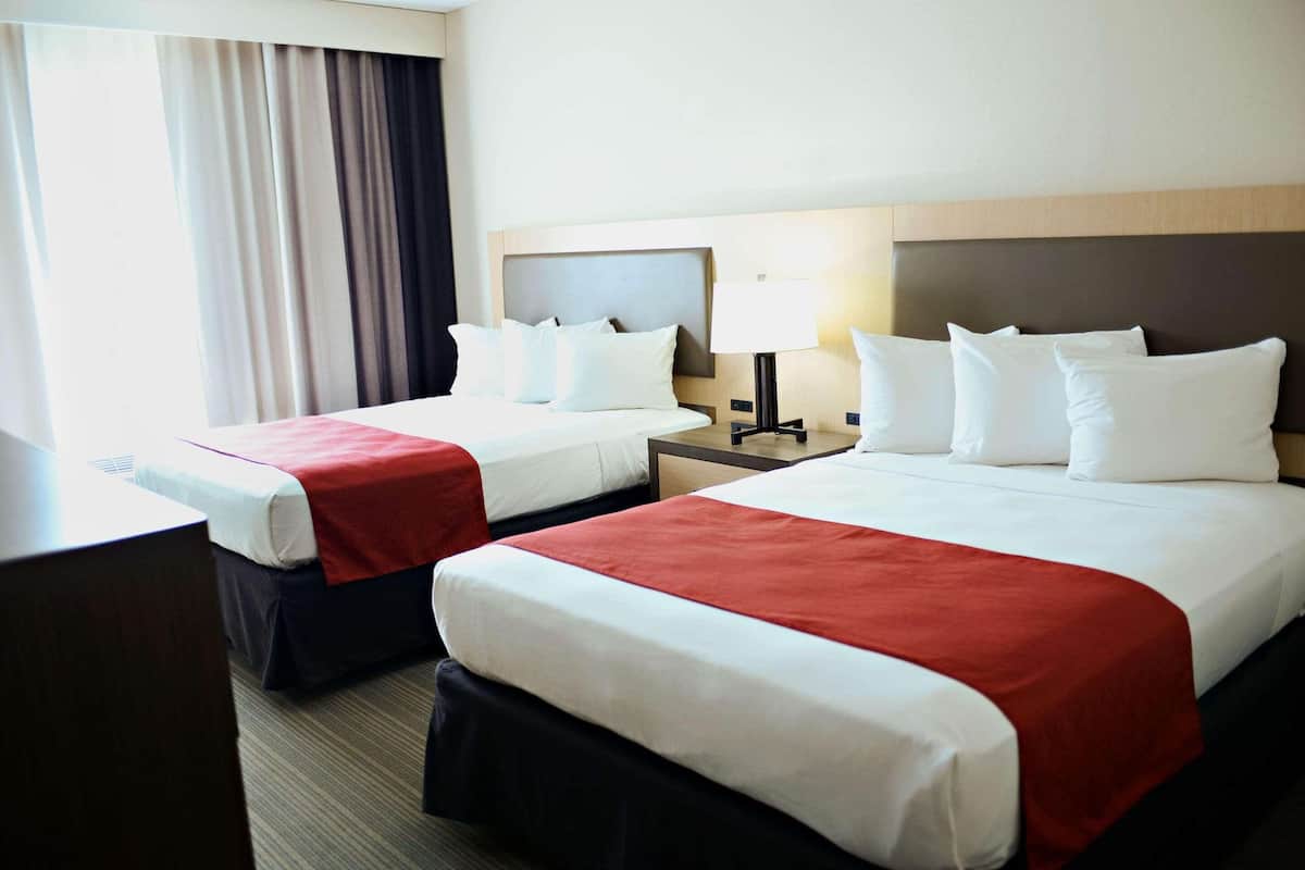 A hotel room with two beds, a desk, a chair, a lamp, and a window with curtains.
