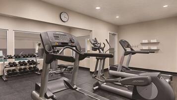 A gym with treadmills, dumbbells, and a clock on the wall.