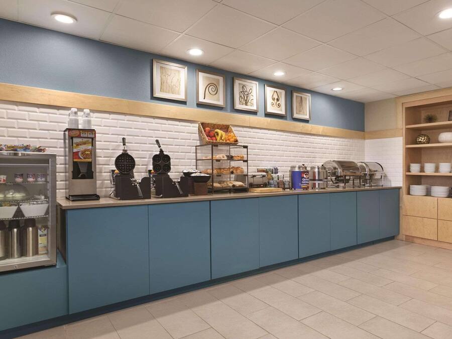 Uma estação de pequeno-almoço com serviço livre, incluindo uma máquina de café, máquina de waffles e diversas opções de comida.