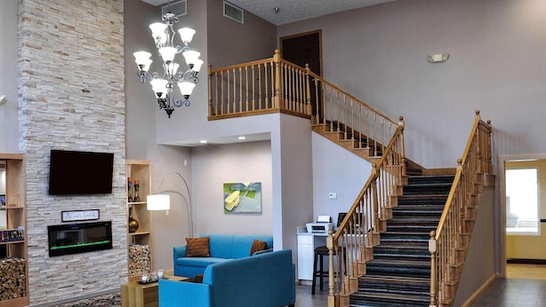 A spacious living area with a blue sofa, a fireplace, a staircase, and a mounted TV. - Country Inn & Suites by Radisson, Beavercreek-Dayton (Dayton)
