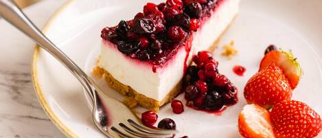 Una rebanada de pastel de queso con frutos rojos sobre un plato, acompañada de fresas y un tenedor.