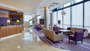 A modern hotel lobby with a reception desk, seating area, and large windows.