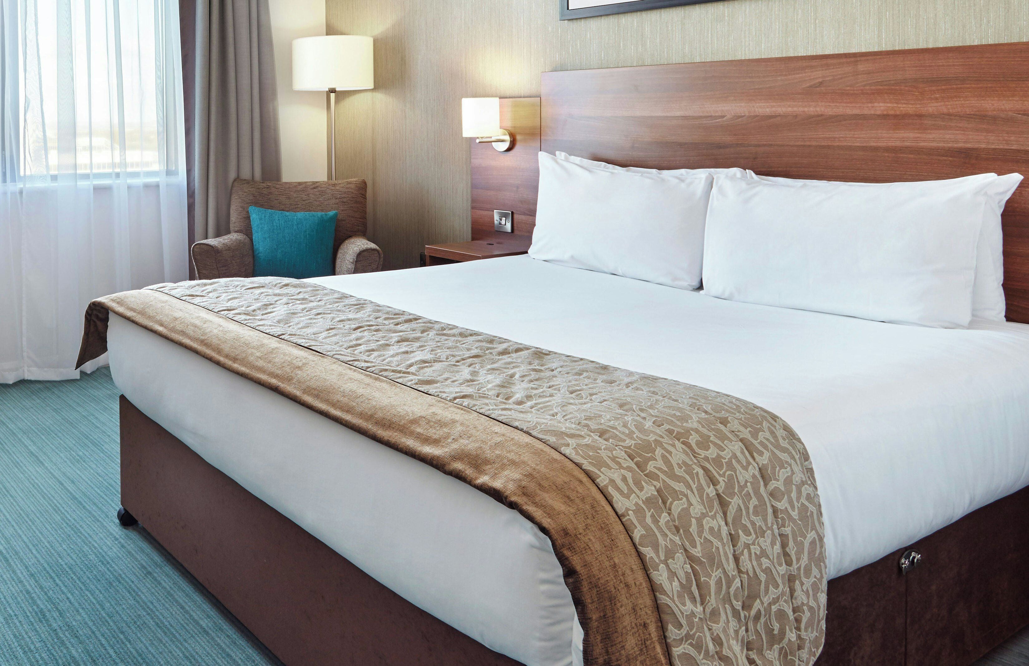 Una habitación de hotel con una cama grande, una silla, una mesita de noche y una lámpara.