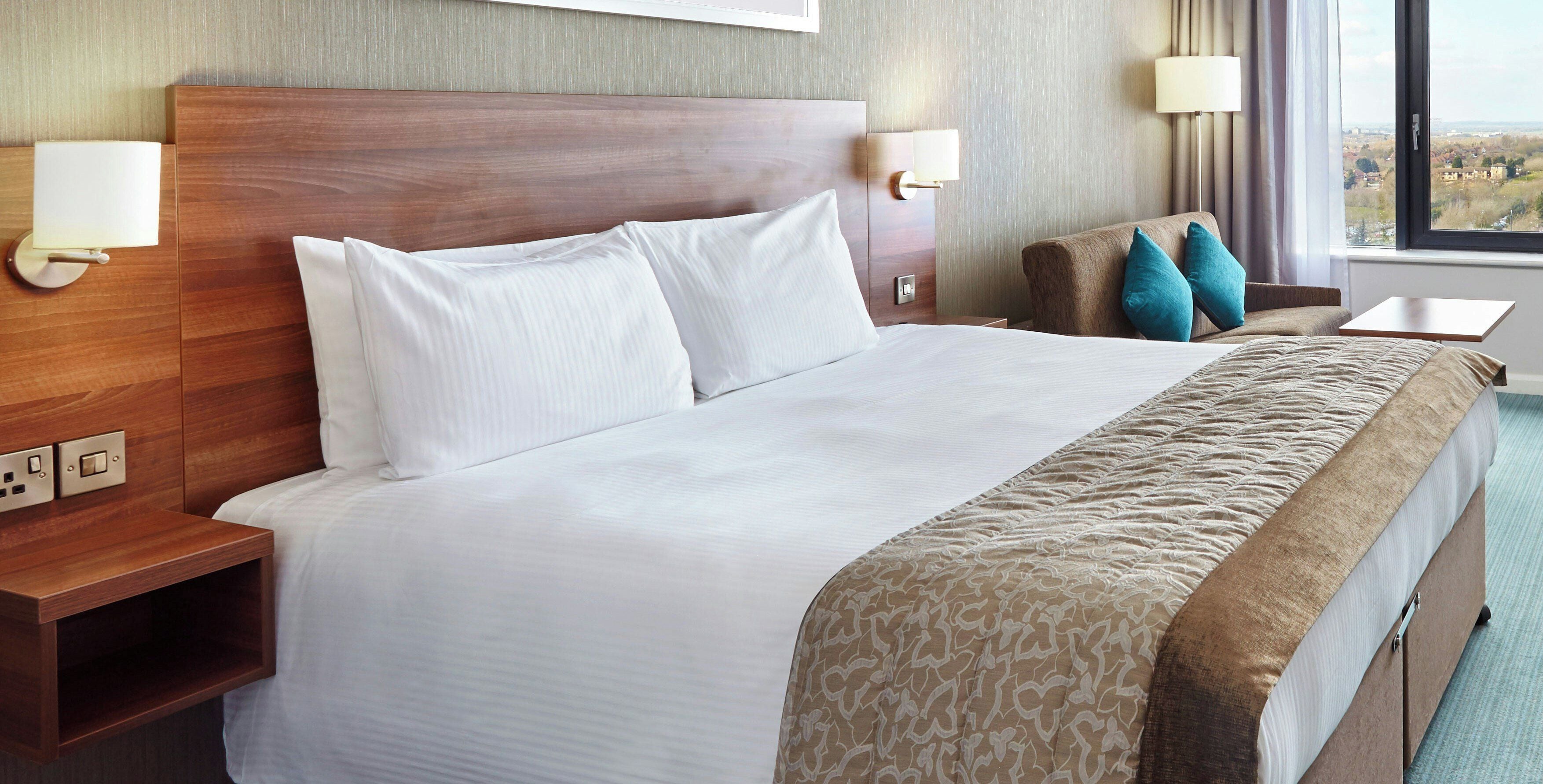 A hotel room with a large bed, two bedside tables, a nightstand, a desk, and a window with a view.