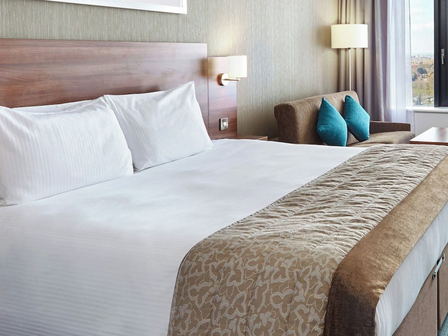 Ein Hotelzimmer mit einem großen Bett, zwei Nachttischen, einem Schreibtisch und einem Fenster mit Blick.