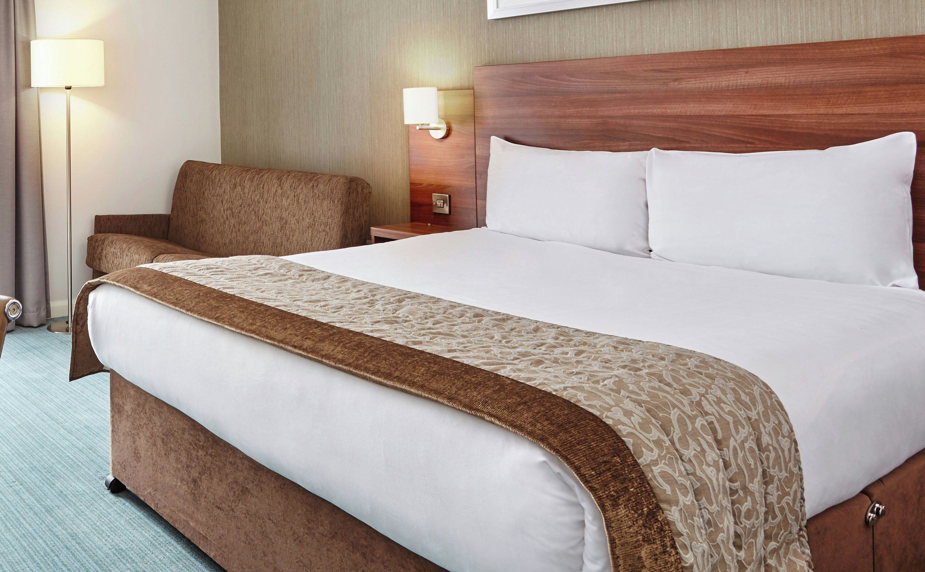 A hotel room with a large bed, a chair, a nightstand, and a lamp.
