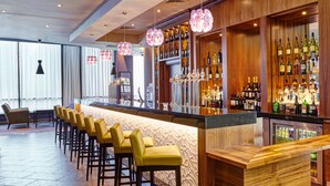 A bar area with a long counter, multiple stools, and a variety of bottles and glasses.