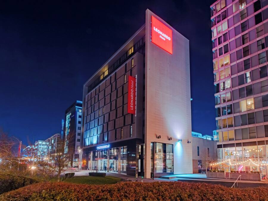 Ein modernes Hotel mit einer auffälligen roten Schrifttafel, mehreren Etagen und einer gut beleuchteten Fassade.