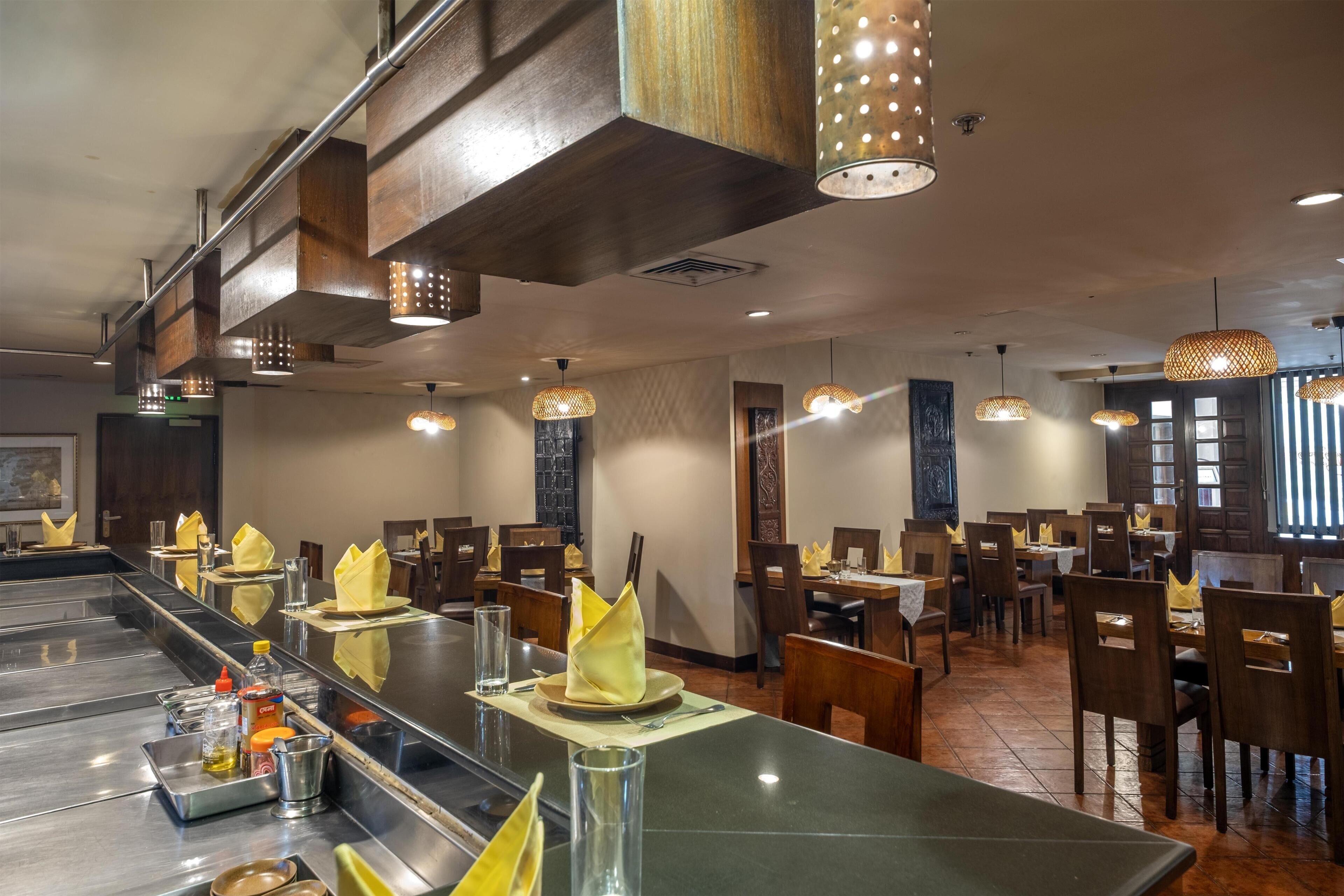 Un restaurante con una barra larga, varias mesas y luces colgantes.