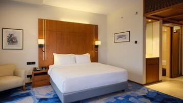 A hotel room with a large bed, bedside tables, a chair, and a wooden headboard.
