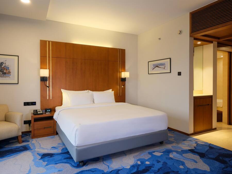 A hotel room with a large bed, bedside tables, a chair, and a wooden headboard.