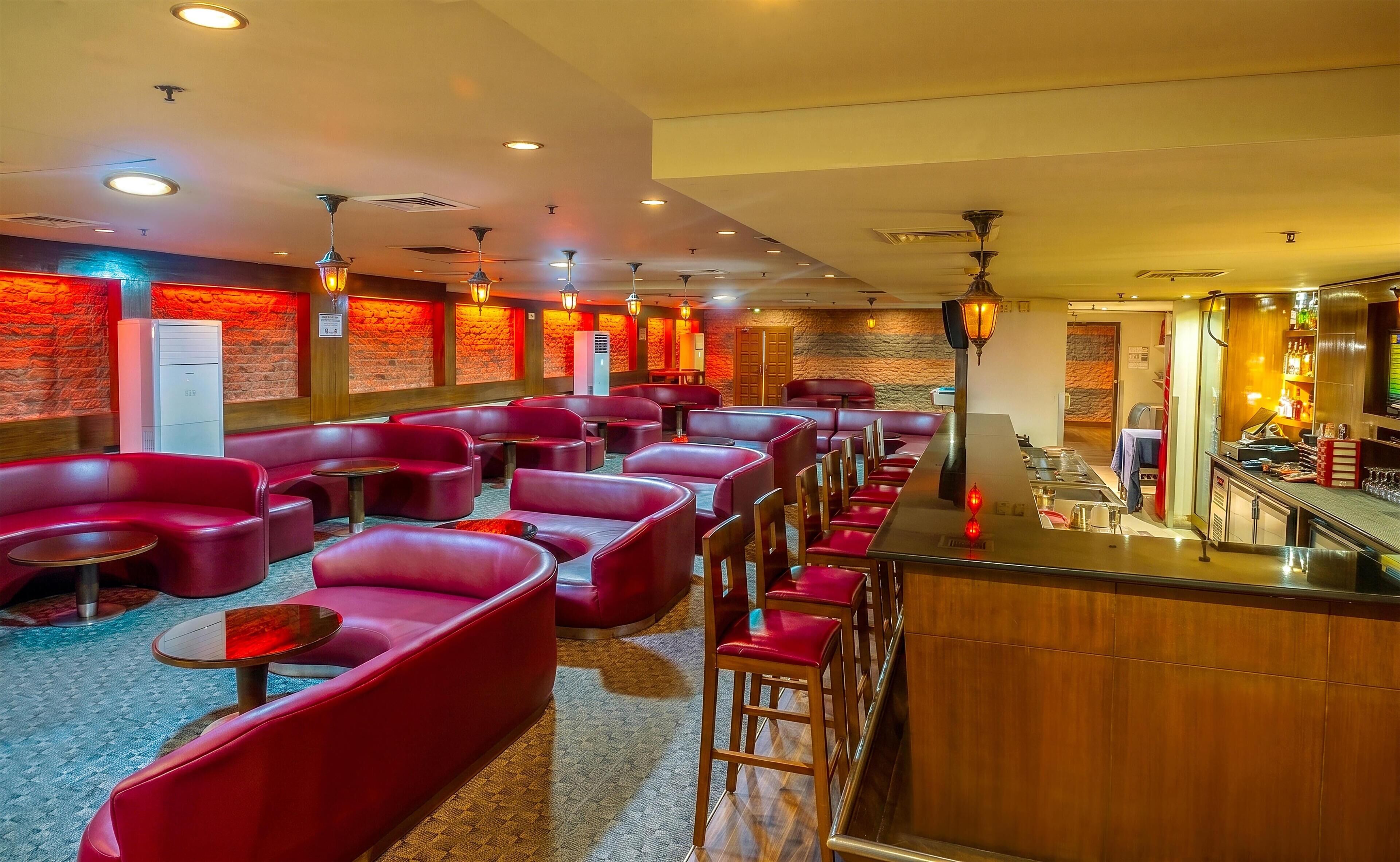 Una hall d'albergo con sedute rosse, un'area bar e una parete in pietra.