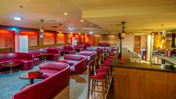 Una hall d'albergo con sedute rosse, un'area bar e una parete in pietra.