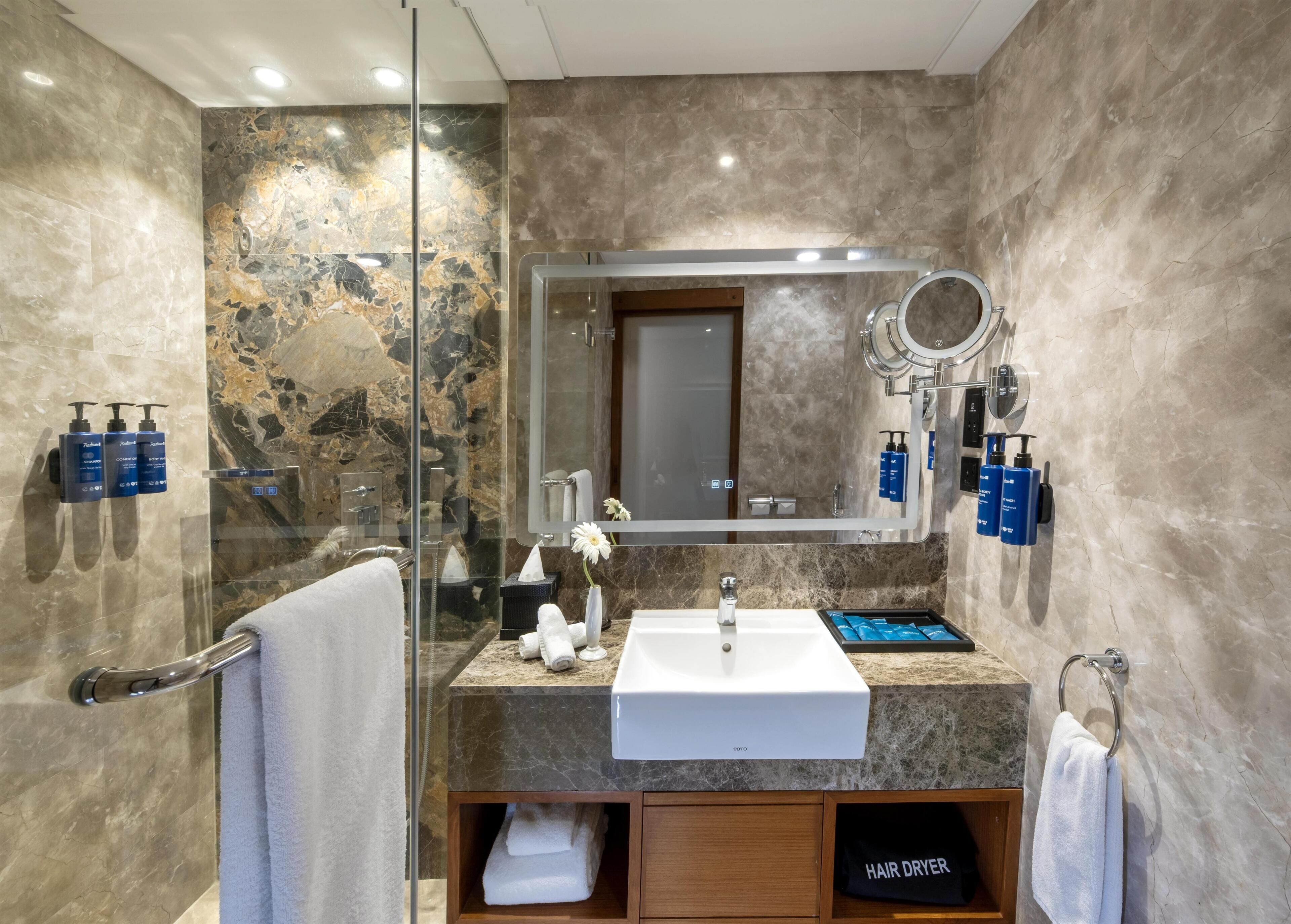 A modern bathroom with a glass shower enclosure, a white sink, and a mirror with a round mirror above it.