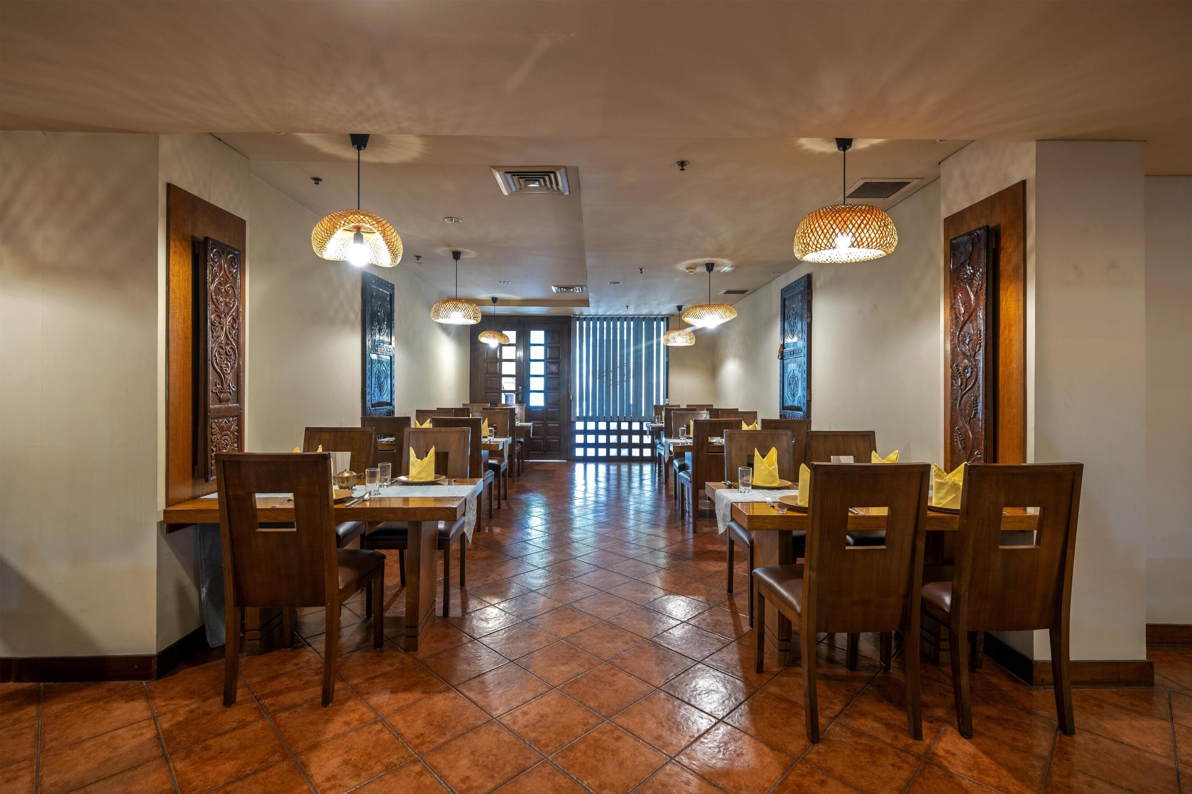 A restaurant with wooden tables and chairs, hanging lights, and a tiled floor.
