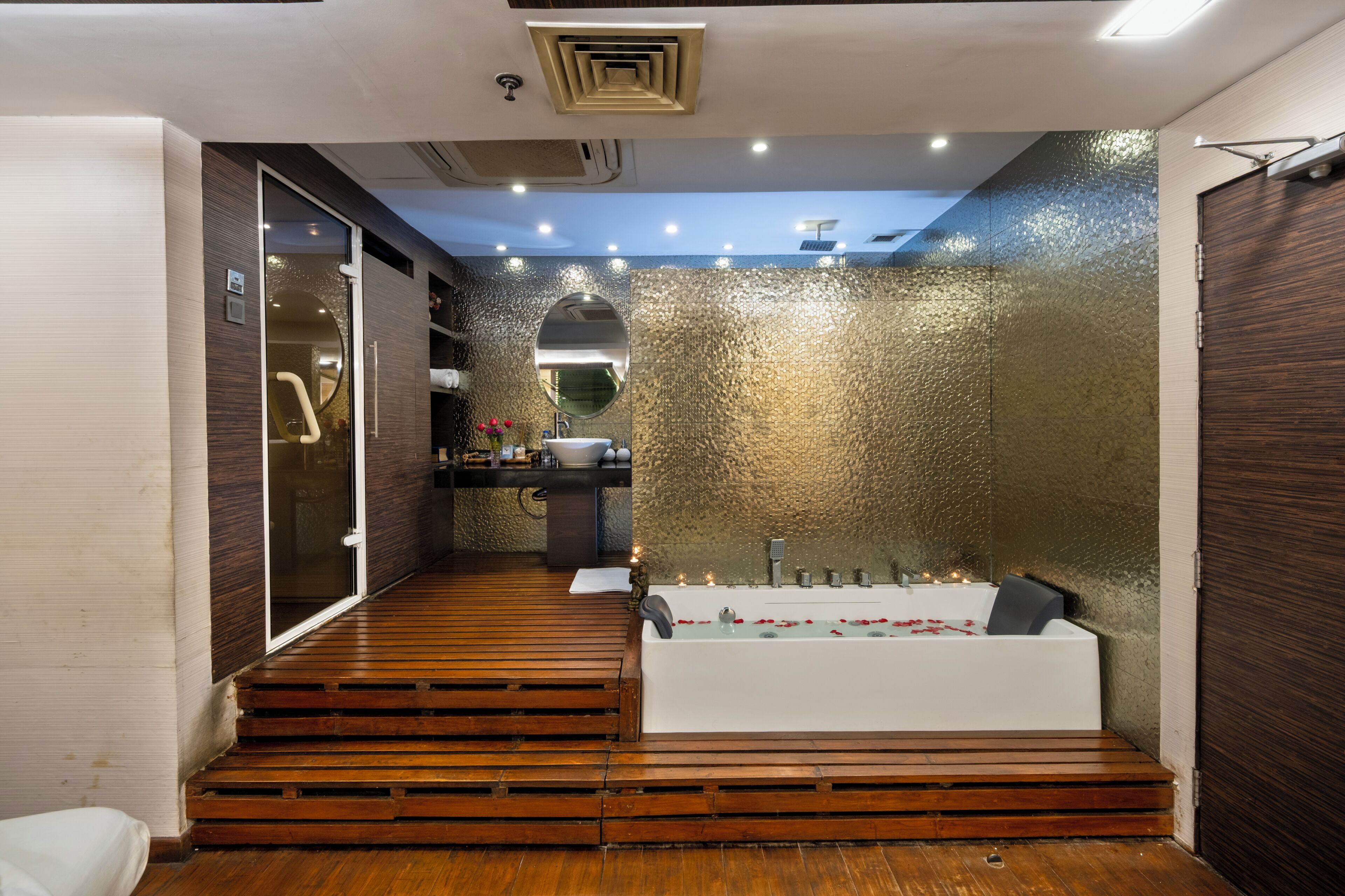 A modern bathroom with a wooden floor, a white bathtub, and a large mirror.