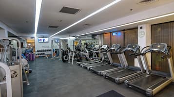 A gym with multiple treadmills, weight machines, and a television screen.