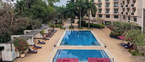 Un hotel con piscina, sillas de descanso y un edificio con balcones.