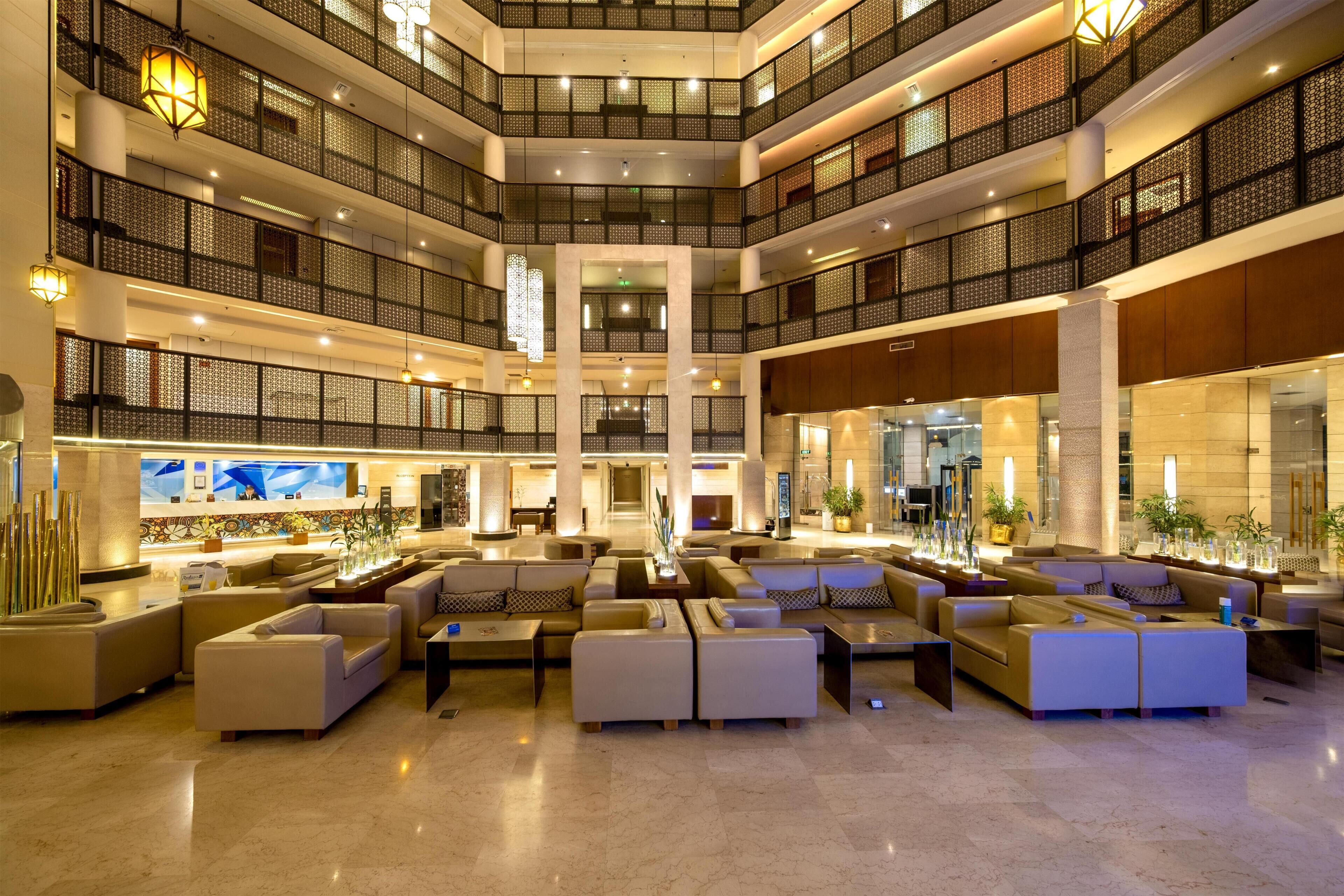 A multi-level hotel lobby with seating areas, a reception desk, and a large chandelier.