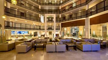 A multi-level hotel lobby with seating areas, a reception desk, and a large chandelier.