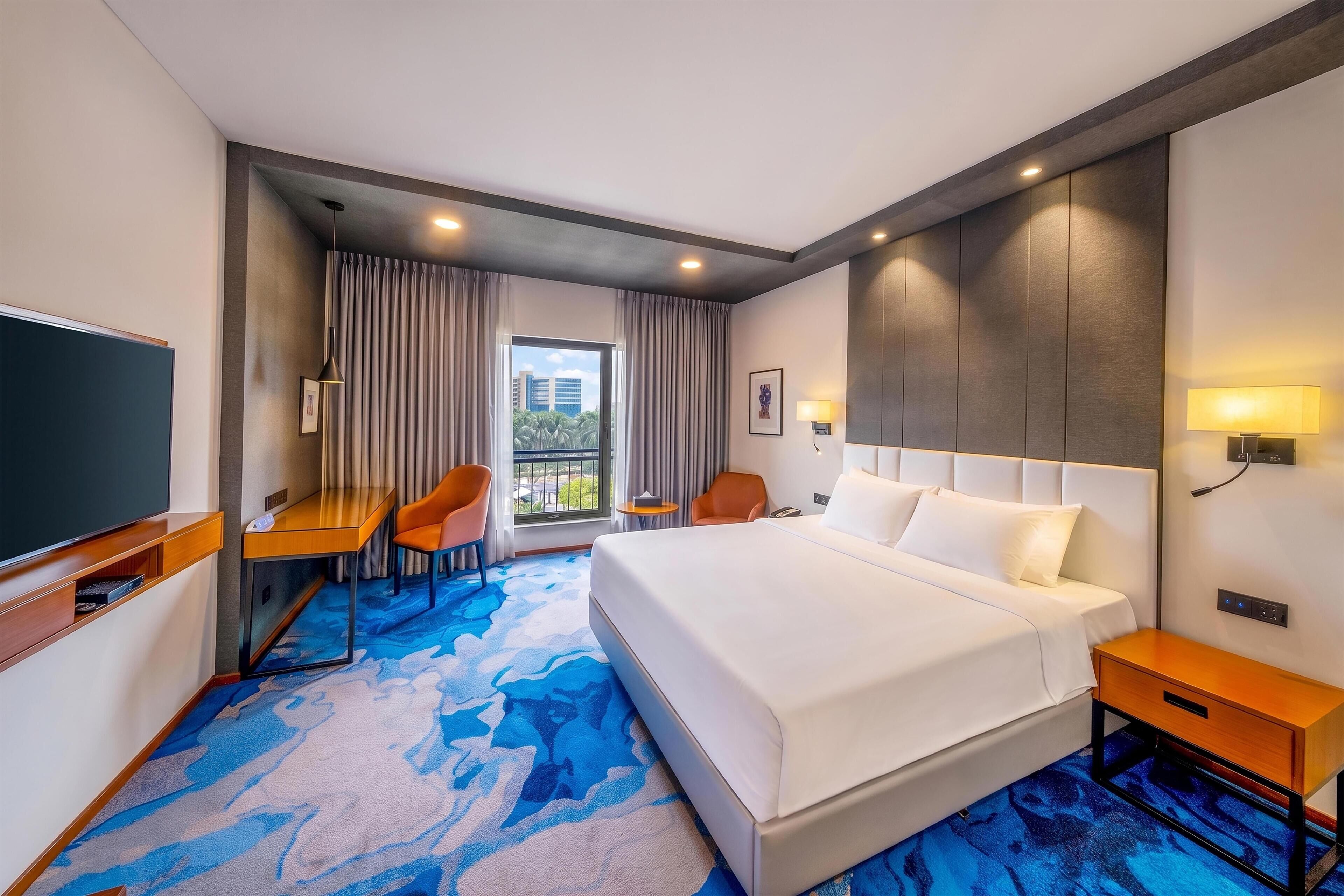 A hotel room with a bed, a desk, a chair, a TV, and a window with curtains.