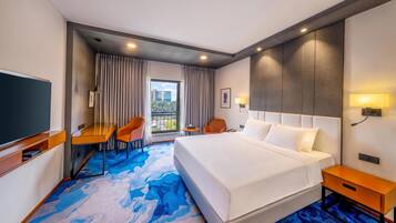 A hotel room with a bed, a desk, a chair, a TV, and a window with curtains.