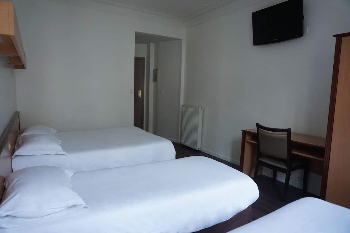 A hotel room with two single beds, a desk, a chair, and a TV on the wall.