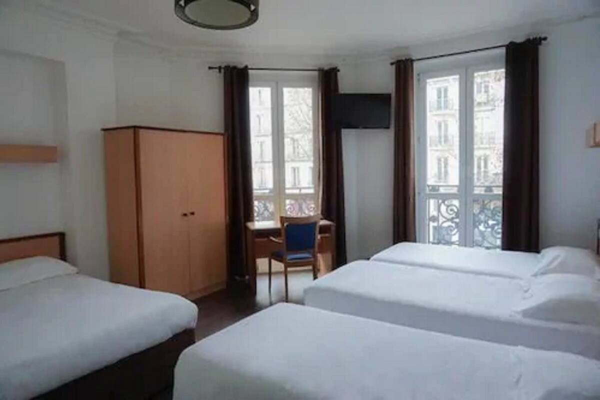 A hotel room with two single beds, a desk, a chair, and a wardrobe.