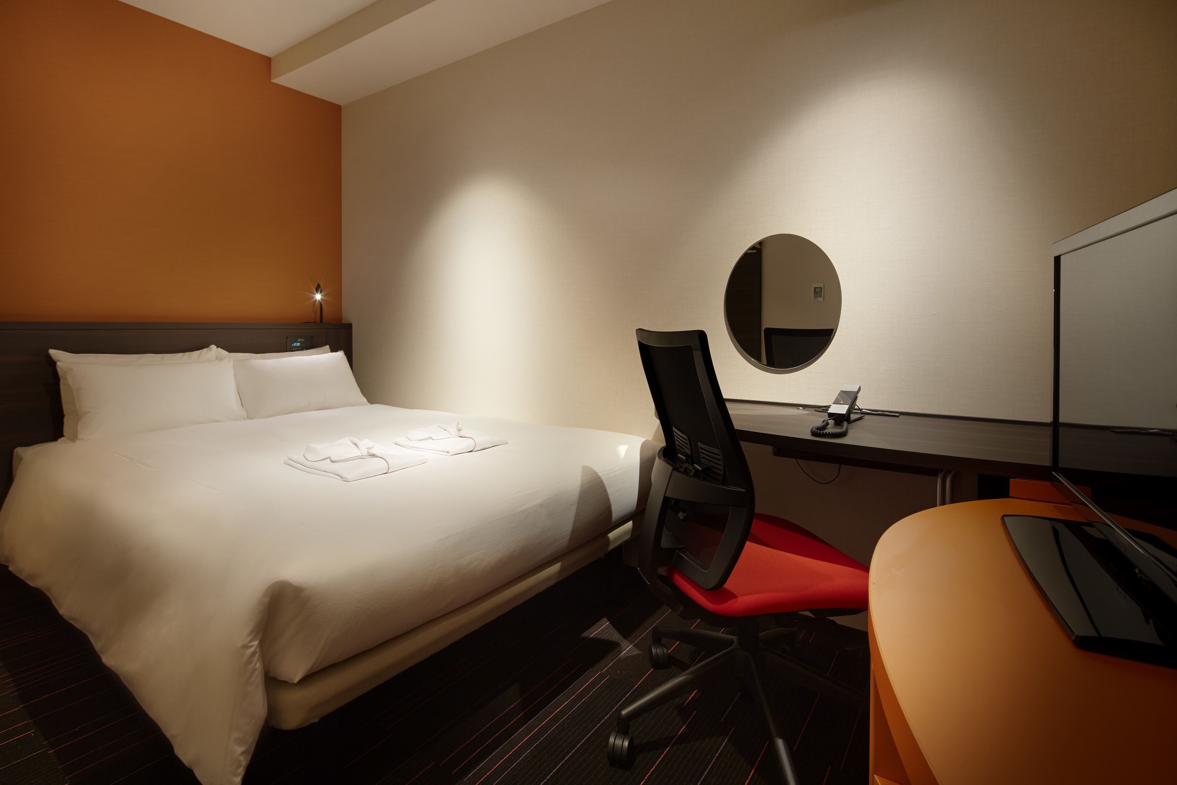 Una habitación de hotel con una cama, un escritorio, una silla, un espejo y un televisor.