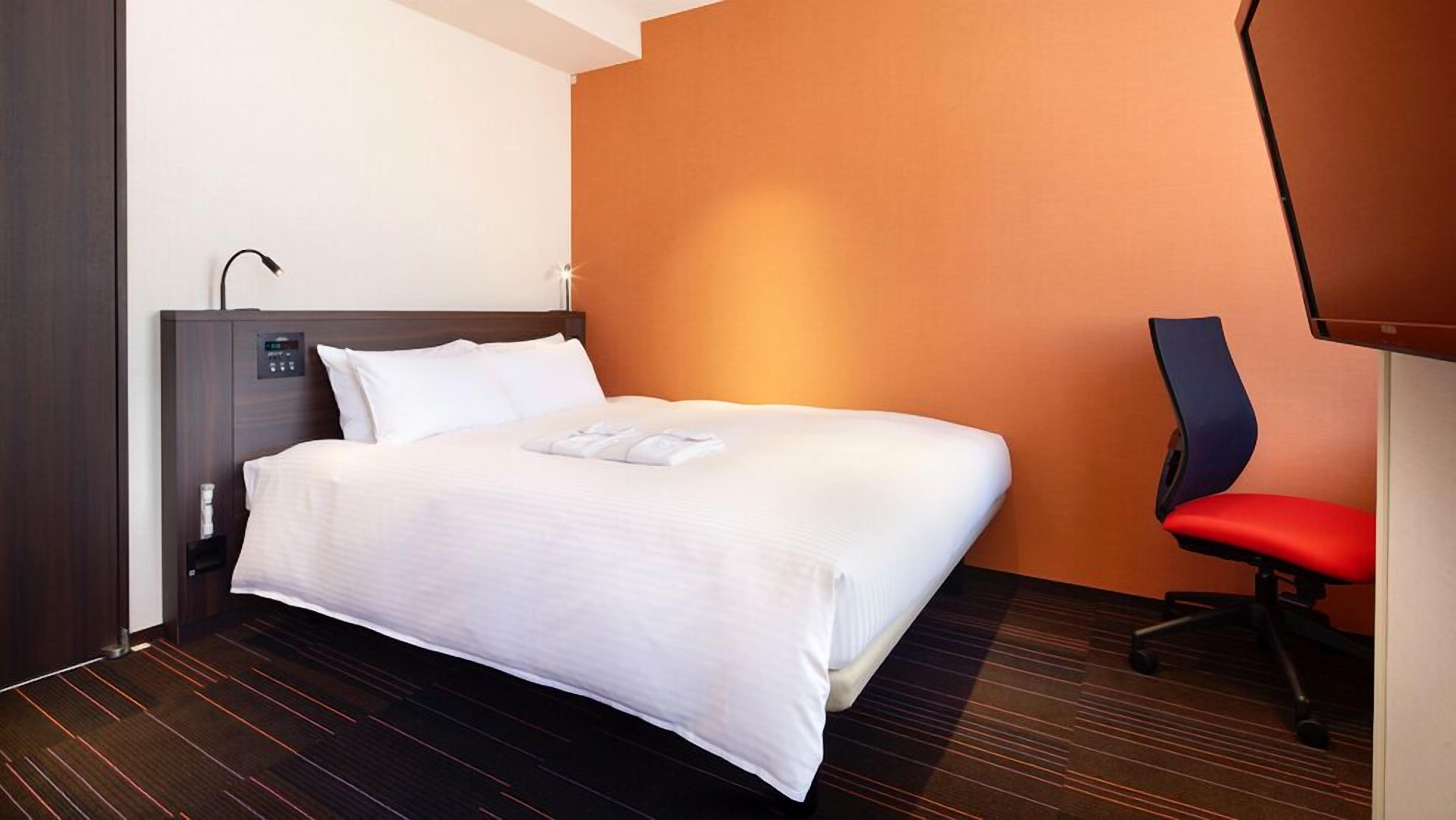 A hotel room with a bed, a desk, and a chair.