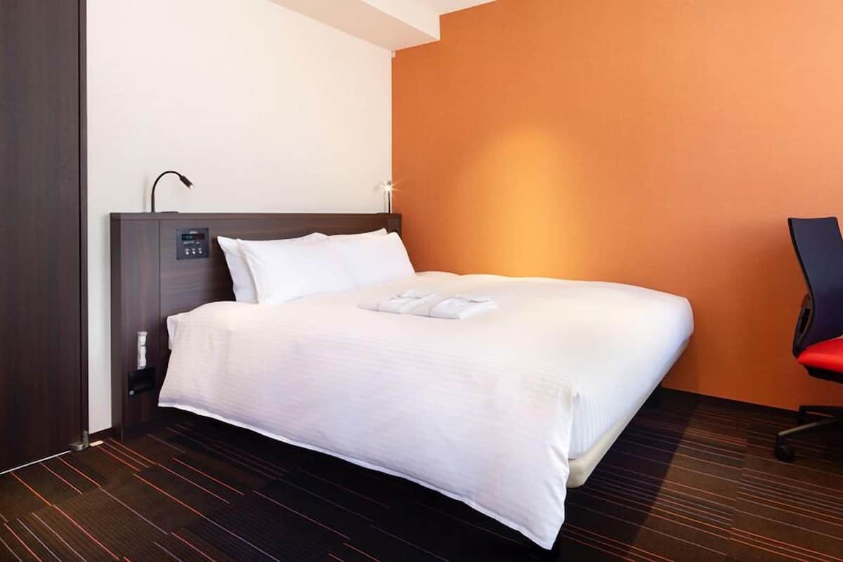 A hotel room with a bed, a desk, and a chair.