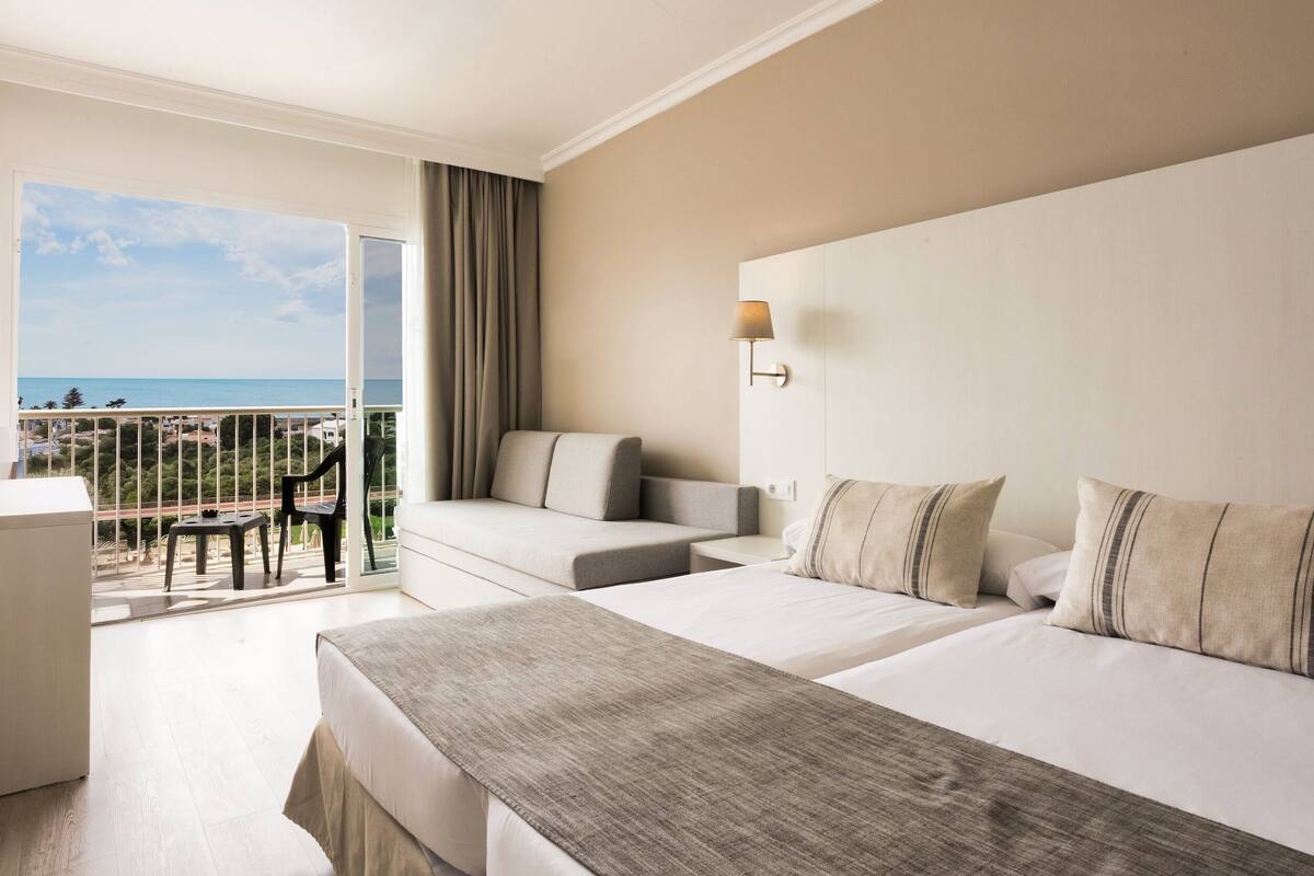 A hotel room with a balcony, a sofa, a bed, and a desk.