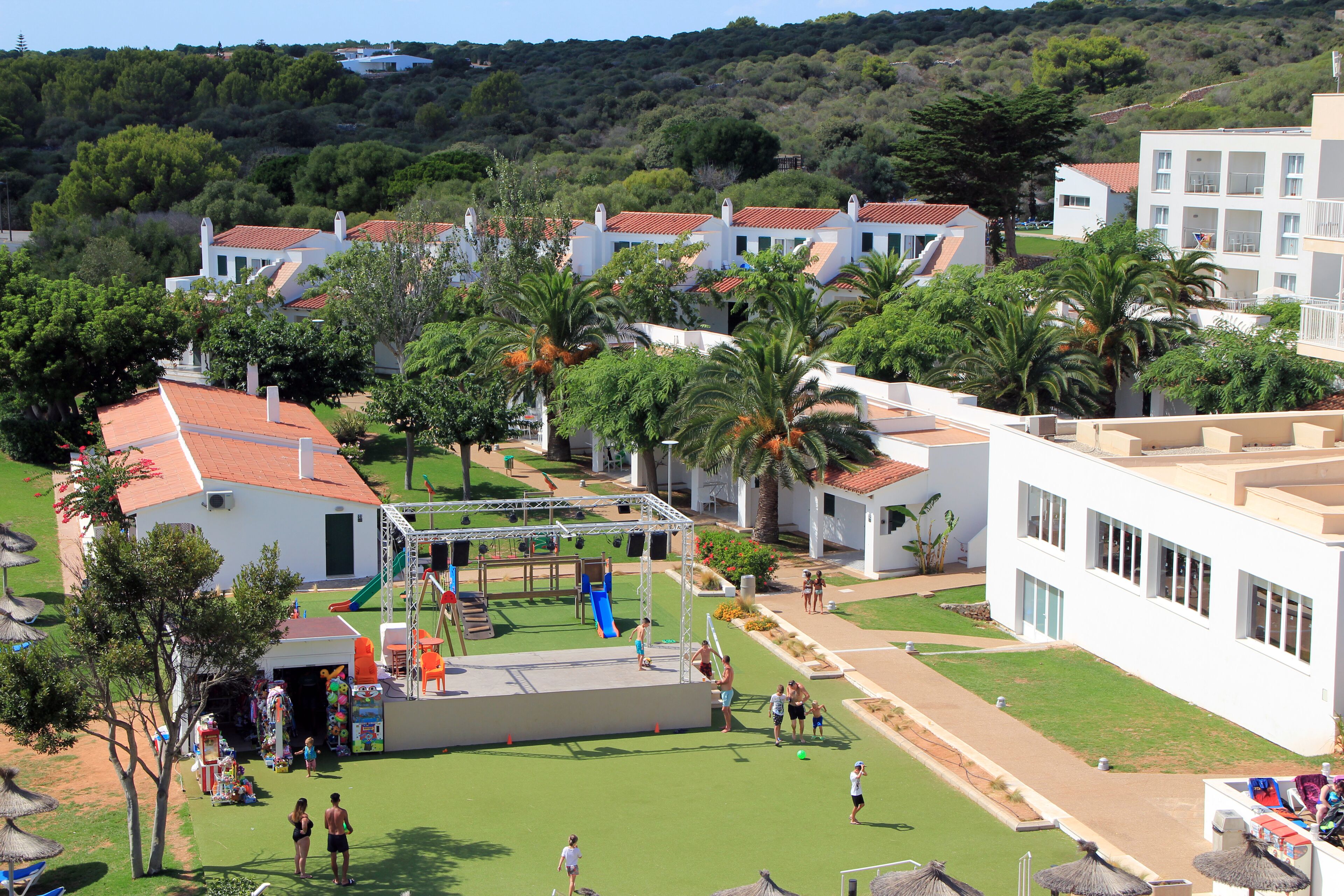Un barrio residencial con edificios blancos, un parque infantil y palmeras.