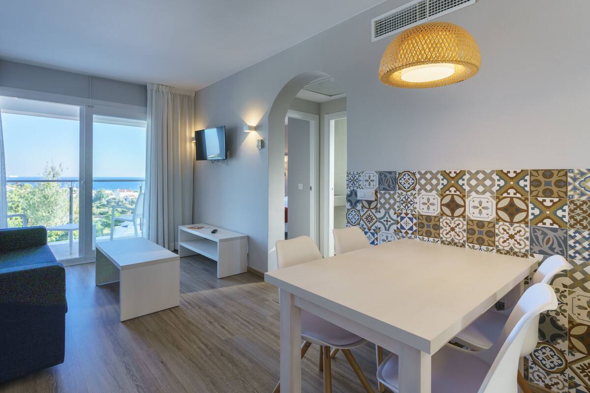 A modern room with a dining table, chairs, a TV, and a balcony with a view.