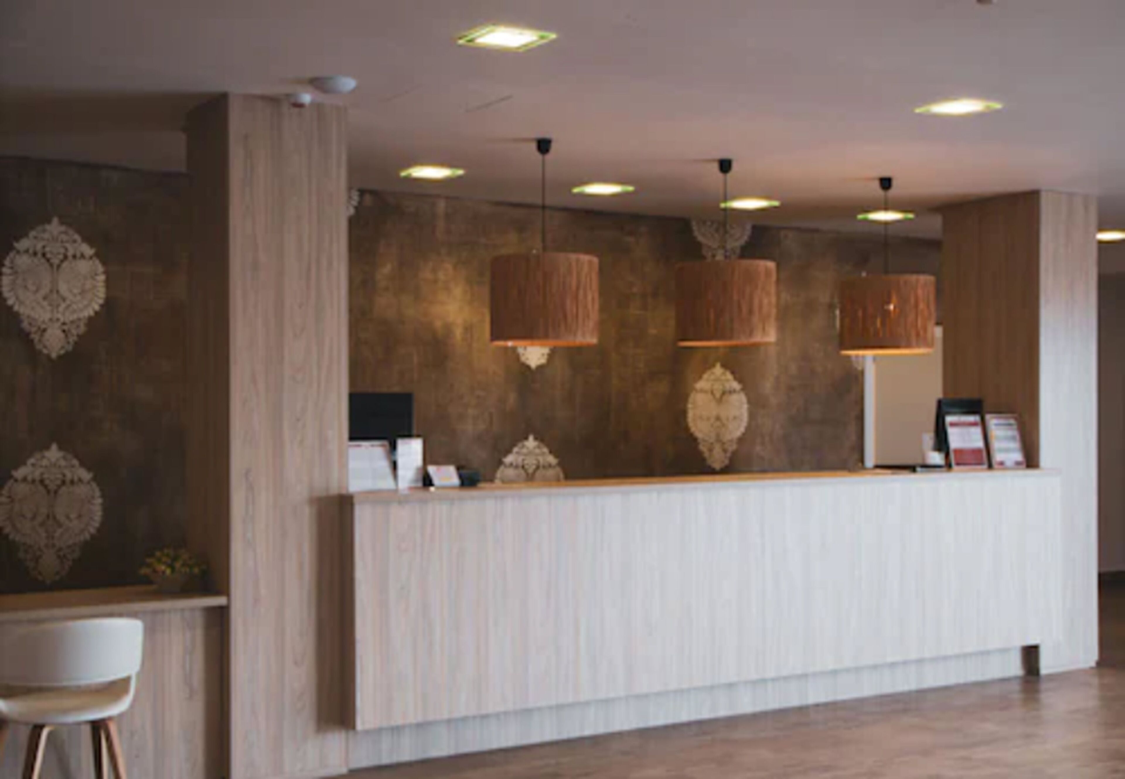Zona de recepción con mostrador de madera, lámparas colgantes y paneles decorativos en la pared.