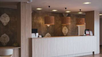 Zona de recepción con mostrador de madera, lámparas colgantes y paneles decorativos en la pared.