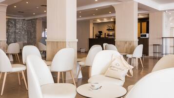 A modern hotel lobby with white chairs and tables, a reception desk, and a bar area.